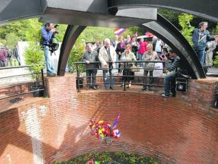 Participantes en el homenaje tiran ramos de flores al interior del pozo Fortuna.
